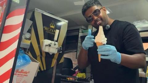 Mr Shuey with a regular ice cream a cone - he has short dark hair, shades, a black T-shirt and blue gloves.