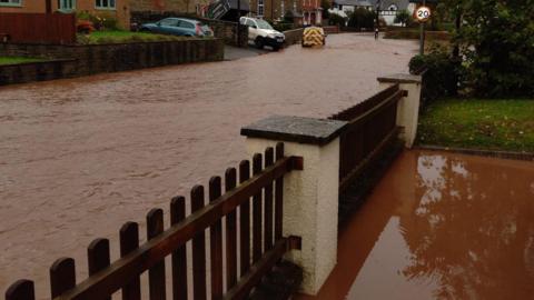 A residential street flooded with dark brown flood water