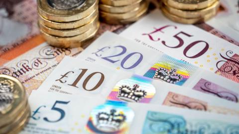 A £5 note, a £10 note, a £20 note and a £50 note laid out next to each other along with several pound coins.