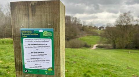 Fixed wooden point in park for members of the public to take pictures. A path and fields can be seen in the background.