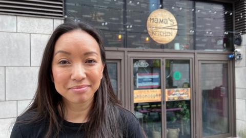 Woman with long dark hair stands in front of business front door with Mama's Kitchen sign in wood.