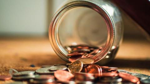 A glass jar with coins falling out of it on to the floor