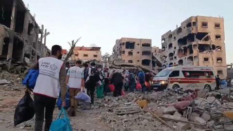 People wearing vests with the name of al-Awda hospital on the back carry bags to a row of ambulances waiting between the rubble of buildings 