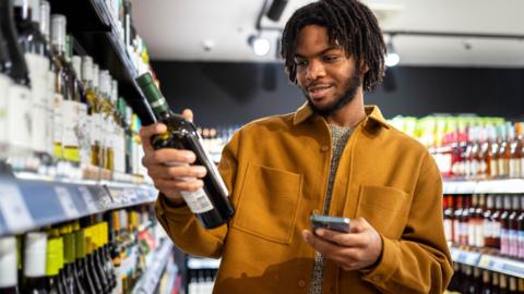A man in a supermarket holding a bottle of wine 