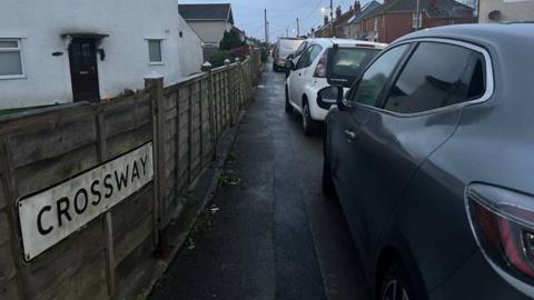 A close up picture of a sign that says Crossway, with cars on the other side of the picture