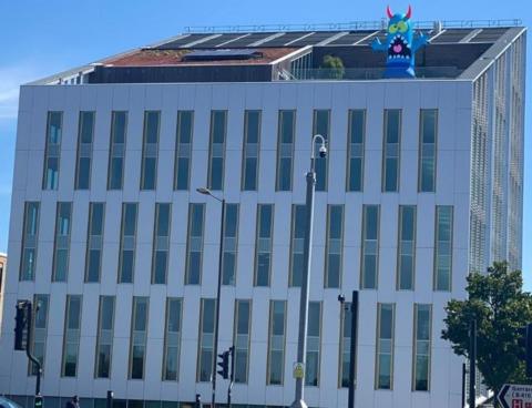 Three rows of rectangular windows up to a slated roof with a blue horned monster with its mouth wide open