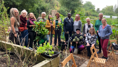 Men and women in a garden in Brierley Hill stand in a row together in the photo. They have plants in front of them and behind and two women are holding plants in their hands.