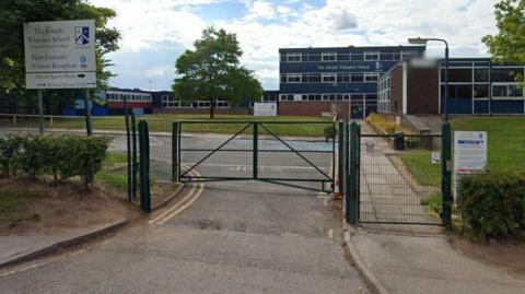 A sign which reads The Joseph Whittaker School with school buildings in the background