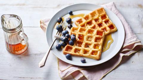 A plate with two waffles and blueberries, topped with maple syrup. 