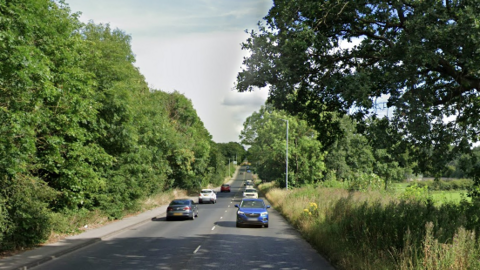 Google streetview image of an A-road with trees and field either side.