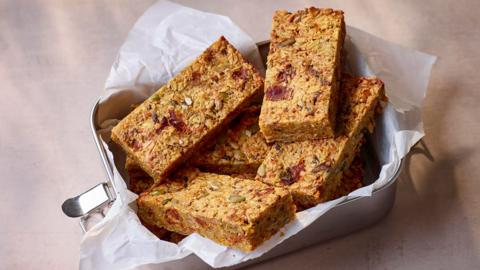 Metal tin filled with savoury flapjacks in baking paper on a beige background
