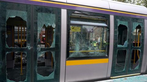 The picture shows a tram with eight windows completed smashed and another cracked