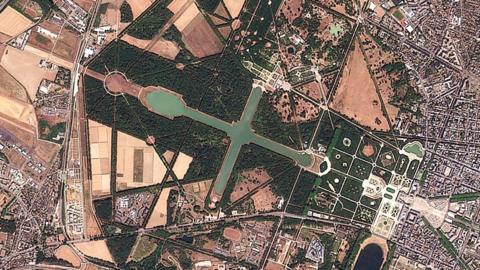 A satellite image showing brown land surrounding the grounds of the Palace of Versailles, which is still filled with greenery