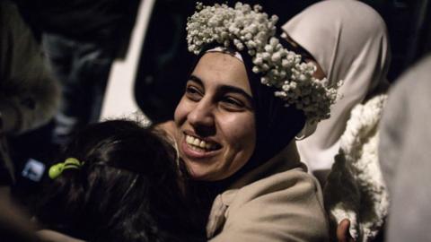 A Palestinian prisoner, wearing a flower crown she received over her headscarf, embraces a young relative upon her arrival