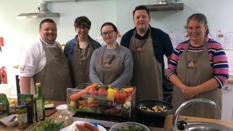 Four cookery students smiling in front of a workspace with chef Ryan from Wiggly