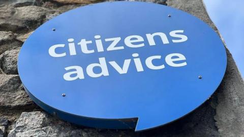 A blue speech bubble sign which says citizens advice sits on a grey stone wall.