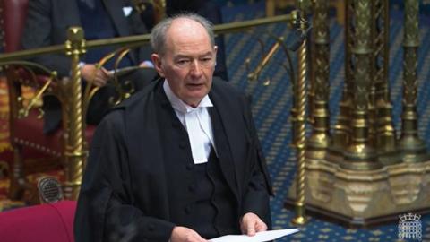 Lord Forsyth dressed in a black cloak and white shirt. He is holding a piece of paper as he addresses the House of Lords.