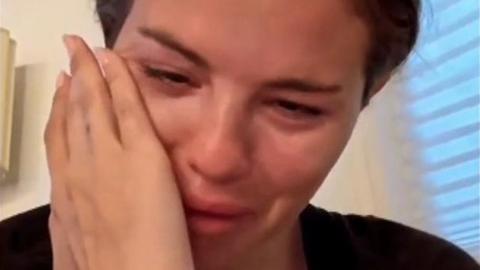 Selena Gomez crying and wiping her face with one hand in a still from her Instagram video