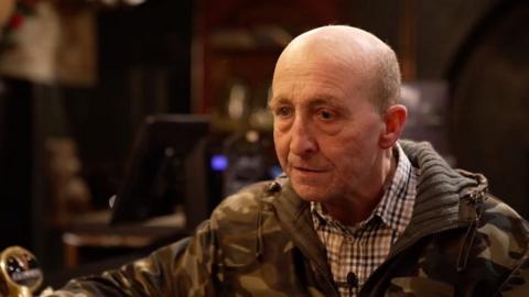 Glen Edwards, who has closely cropped hair, wearing a jacket in combat colours and a brown chequered shirt with a collar.