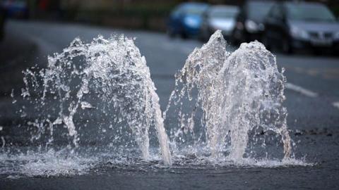 Water spurts upwards out of a drain on a road.