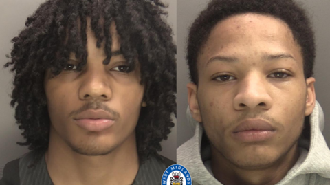 A composite image of two young men in police mugshots. The one on the left has dark brown dreadlocks, dark brown eyes, and a faint black beard and moustache. He is wearing a black football shirt with round neck and has a serious expression. The young man on the right has black hair, a face marked with spots, dark brown hair and eyes and also has a sober expression.