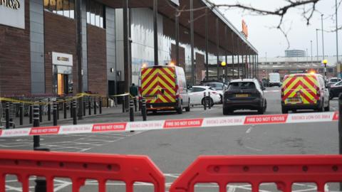 Ambulances and emergency cars parked outside the Marks and Spencer building with a red and white police tape.