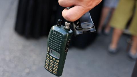 A walkie talkie is held by a male hand with the battery taken out, as a precaution amid exploding devices around the country, at a funeral in Beirut on 18 September