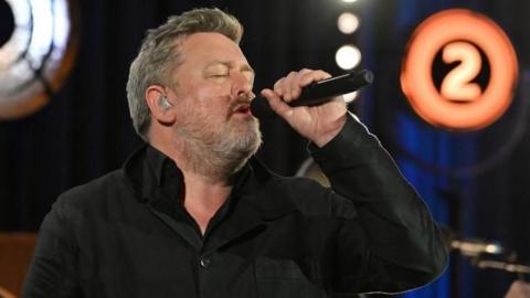 Elbow lead singer Guy Garvey, wearing a black shirt, performs holding a microphone