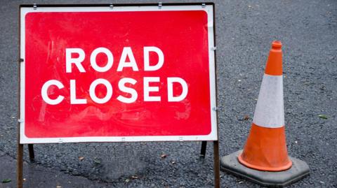 A road closed sign next to a traffic cone