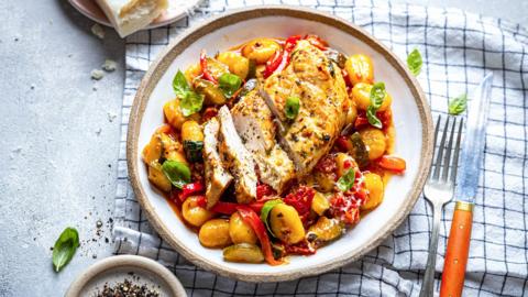 Sliced chicken breast on top of vegetables and gnocchi, on a white plate.