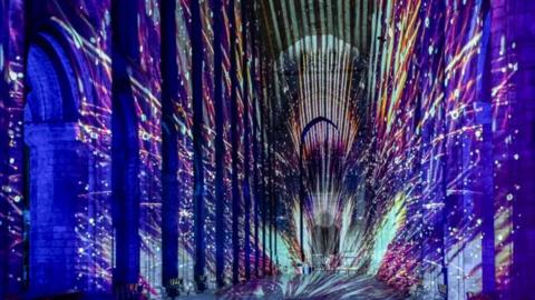 The inside of Ely Cathedral is covered with lights which are projecting on to the building and are showing multiple colours.  