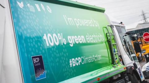 A blue and green bin lorry in BCP that says 'I'm powered by 100% green electricity' on it.