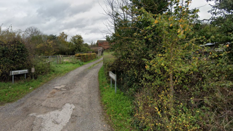 The ramshackle entrance to a road bordered by overgrown hedgerows