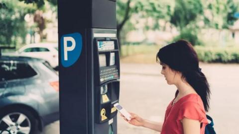 A woman looks down at her mobile phone as she starts next to a parking payment machine