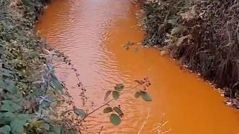 Water in the River Calder at Todmorden which is heavily discoloured making it appear to be orange