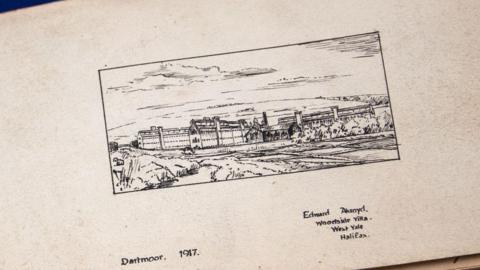 A pen and ink drawing of Dartmoor Prison on a yellowing page in the album. It includes the caption Dartmoor 1917