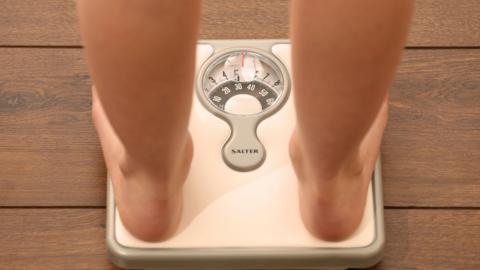A generic image of a person standing on a pair of silver weight scales. You can see their bare legs and feet.