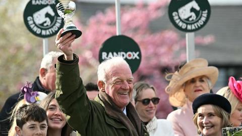 Willie Mullins smiling and holding a trophy in the air
