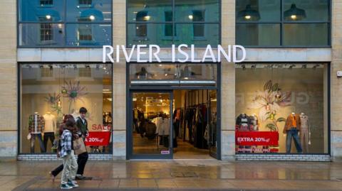 People walk outside River Island store on high street