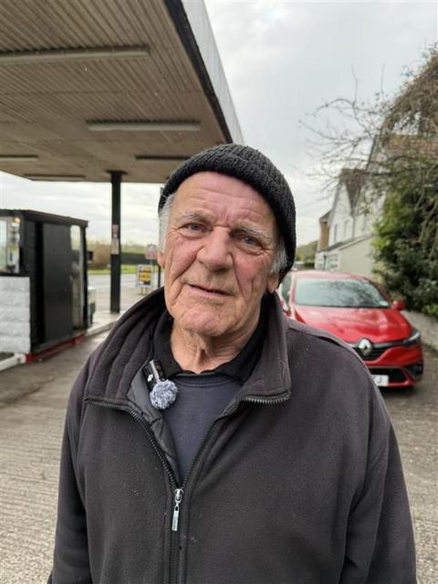 Man in black fleece and hat standing in a forecourt