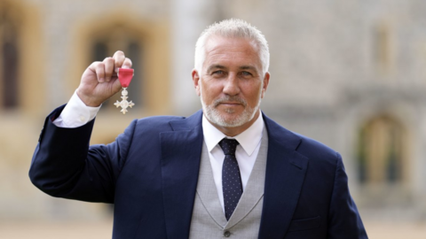 Paul Hollywood holds up MBE after being honoured at a ceremony at Windsor Castle