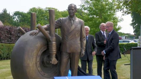 Statue of man being unveiled by gentlemen in black suits.