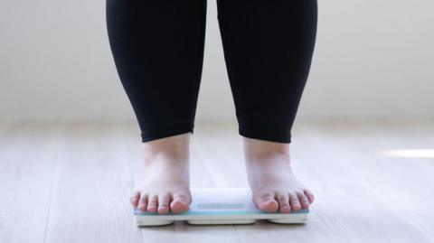 An anonymous woman who is overweight stands on some weighing scales