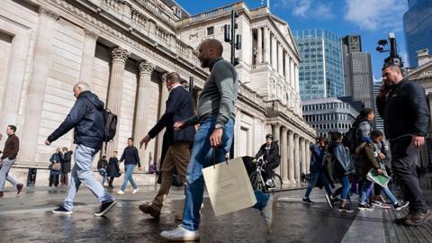 People walk down the street carrying bags in front of the Bank of England in London in OCtober