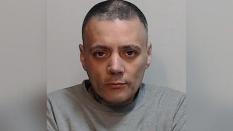 Patrick Moohan staring straight at the camera. He has short, dark hair. He has dark eyes. He is wearing a grey jumper and standing against a grey background.