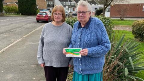 Two elderly women. They are outside their house.
