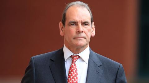 Former West Yorkshire and Merseyside chief constable Sir Norman Bettison leaves Preston Crown Court in 2017. He wears a grey suit with a white shirt and a red tie