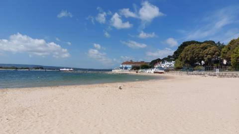 SUNDAY - A sunny beach at Sandbanks with the blue Sandbanks Hotel and the Sandbanks Ferry in the background