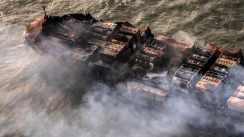 Smoke emitting from a semi-burnt out cargo vessel, which is drifting in the sea.