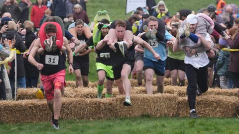 Several men race with women hanging from their backs. 
